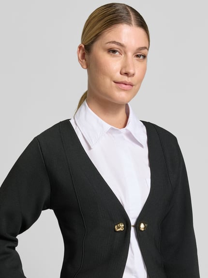 Frauenmodel trägt schwarzen Cardigan mit goldfarbenen Zierknöpfen, V-Ausschnitt, gerader Schnitt, Produktname 'Cardigan mit Zierknöpfen Modell APOLLO' von MANGO, Nahaufnahme Oberkörper