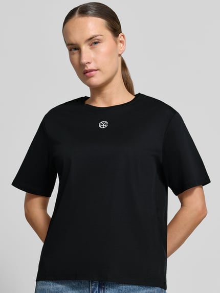 Frauenmodel trägt Regular Fit T-Shirt aus reiner Baumwolle Modell 'Melea' von MSCH Copenhagen, Schwarz, Logo-Print, Nahaufnahme Oberkörper.