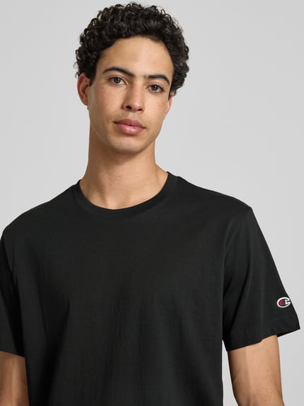 Męski model nosi T-Shirt mit Rundhalsausschnitt im 2er-Pack od CHAMPION, czarny, krój regular fit, bawełna, detal z logo, zbliżenie na górną część ciała.