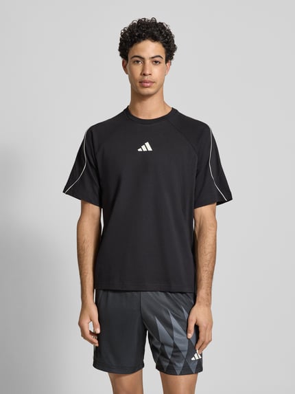 Männermodel trägt T-Shirt mit Label-Print von adidas Sportswear, schwarze Baumwolle, Regular-Fit, gerippter Rundhalsausschnitt, Ganzkörperansicht von vorne.