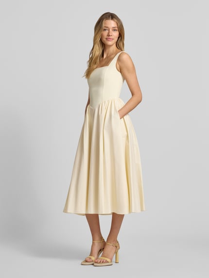 Frauenmodel trägt Cocktailkleid mit rückseitigem Reißverschluss von Jake*s Cocktail aus Baumwoll-Mix mit Stretch-Anteil, A-Linie, Midikleid, sanft glänzender cremefarbener Stoff, glatte Textur, Ganzkörperansicht von vorne. Rückenlänge bei Größe 36: 123 cm, Brustweite: 40 cm.
