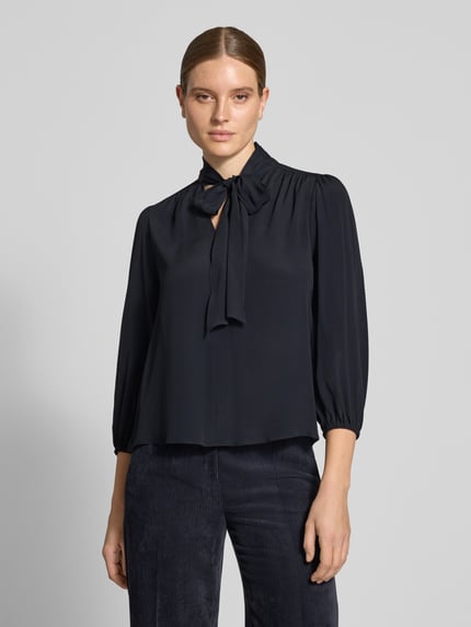 Modelka nosi Relaxed Fit Bluse mit Seiden-Anteil od Luisa Cerano, czarny Acetat-Mix z ozdobną kokardą, rękaw o dł. 3/4, długość tyłu 62 cm, długość rękawów 50 cm, widok całej sylwetki z przodu.