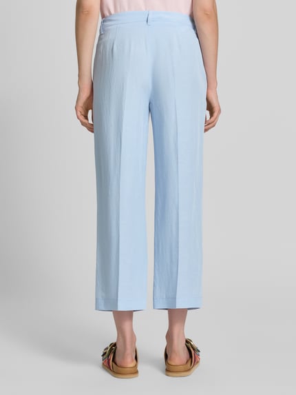 Frauenmodel trägt Stoffhose mit Bügelfalten Modell 'OLESSA' von Raffaello Rossi, hellblau, glatte Textur, 7/8 Fit, Ganzkörperansicht Rückansicht. Viskose-Mix mit Leinen-Anteil, Haken- und Reißverschluss, französische Eingrifftaschen.