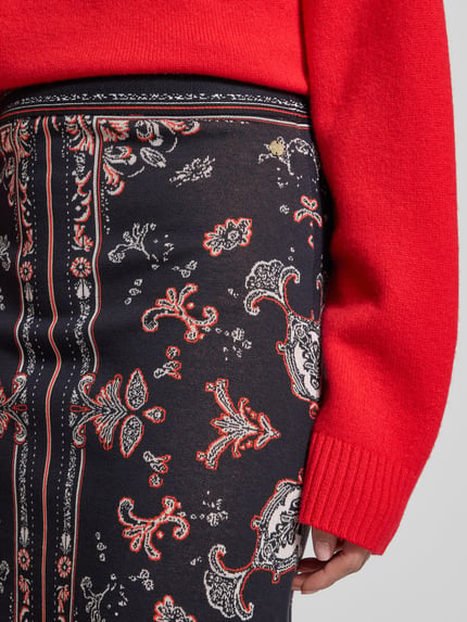 Frauenmodel trägt Knielanger Strickrock im Allover-Look von Marc Cain, Baumwoll-Viskose-Mix mit Paisley-Muster, Nahaufnahme Oberkörper.