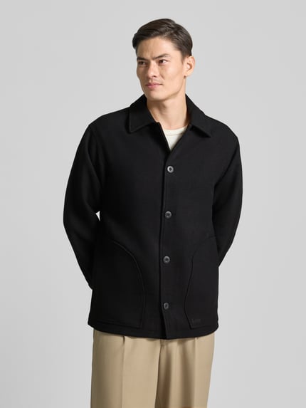 Männermodel trägt Jacke mit Umlegekragen und Knopfleiste Modell 'CAVE' von Forét, Regular Fit, schwarzer Baumwoll-Mix, Ganzkörperansicht von vorne.