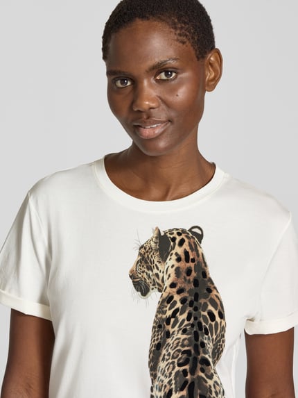 Frauenmodel trägt T-Shirt mit großem Motiv von MARC CAIN, mehrfarbiges Motiv-Print auf weißem Jersey, Rundhals, Kurzarm, Nahaufnahme Oberkörper.