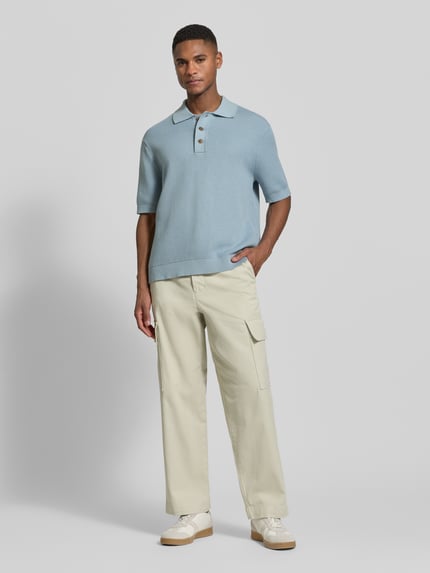 Männermodel trägt Relaxed Fit Poloshirt aus reiner Baumwolle Modell 'DANE' von SELECTED HOMME in Hellblau, Strickoptik, Ganzkörperansicht von vorne.