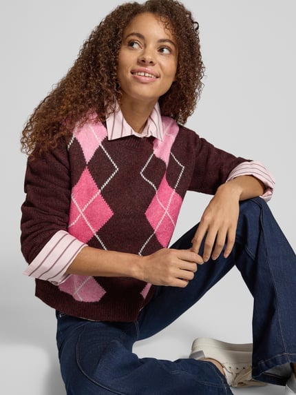 Vrouwenmodel draagt Relaxed Fit gebreide pullover uit Wolmix Model 'HARVI' van JJXX, ruitmotief, ruglengte maat S 50 cm, mouwlengte 57 cm, kleur bruin en roze, Ganzkörperansicht von vorne.