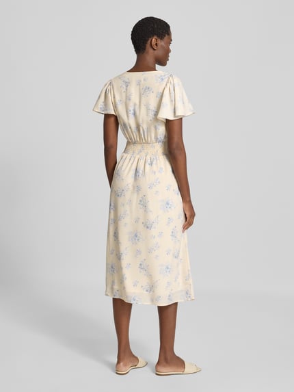 Frauenmodel trägt Midikleid mit Knopfleiste Modell 'Eleni' von Neo Noir in Creme mit blauem Allover-Blumenmuster, A-Linie, Ganzkörperansicht Rückansicht.