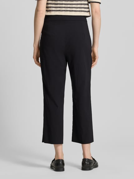 Vrouwenmodel draagt Hose aus Viskose-Mix in verkürzter Passform Modell 'FENJA2' van STEHMANN in zwart, rechte pijpen, elastische tailleband, viscosemix met stretch, verkorte fit, detail van de bandmaat en binnenbeenlengte bij maat 36, volledige lichaamsweergave achteraan.