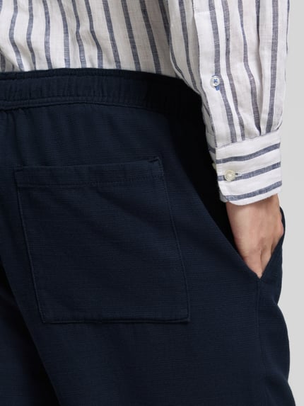Mężczyzna nosi Shorts aus Baumwolle mit elastischem Bund od JAKE*S STUDIO MEN, granatowy kolor, krój regular fit, detal tylnej kieszeni, zbliżenie na biodro