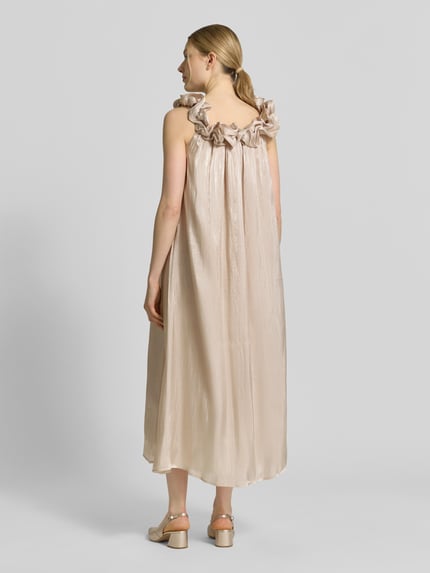 Frauenmodel trägt Relaxed Fit Midikleid mit Zierbesatz Modell 'Turino' von YAS, glänzende beige Textur, ärmellos, Ganzkörperansicht Rückansicht.