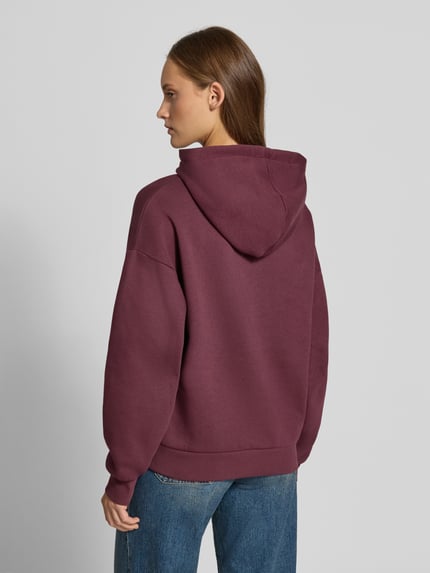 Frauenmodel trägt Relaxed Fit Hoodie aus Baumwoll-Mix Modell 'VESTERBRO' von JJXX in dunklem Bordeaux, strukturierte Optik, Ganzkörperansicht Rückansicht. Damen Hoodie, Känguru-Tasche, Kapuze mit Tunnelzug, Label-Detail.