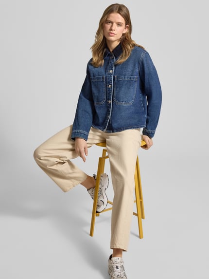 Vrouwenmodel draagt Oversized Jeansjacke aus Baumwoll-Mix Modell 'CASSIE' van Only in uni-denimkleur, relaxed fit, borstzakken, omlegekraag, enkelvoudige knopenrij, borstpas, lange mouw met manchet, afgeronde zoom, cord details, materiaalverwerking denim en katoenmix. Volledige lichaamsweergave van voren.