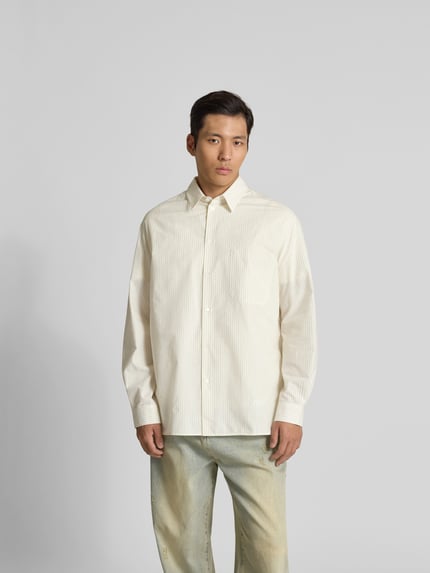 Męski model nosi Oversized Freizeithemd mit Kentkragen von MAISON KITSUNÉ, kremowe paski, brustasza, listwa guzikowa, z długim rękawem, długość tyłu w rozmiarze M: 82 cm, szerokość ramion w rozmiarze M: 48 cm, długość rękawów w rozmiarze M: 64 cm, całkowity przód, koszula casualowa, krój oversized, kołnierzyk typu kent, gładka tekstura