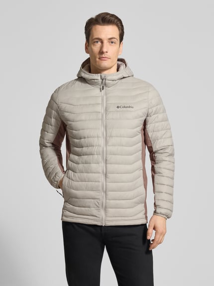 Männermodel trägt Steppjacke mit Kapuze und Logo von Columbia in Beige mit Regular-Fit, Reißverschluss, Ganzkörperansicht von vorne. Rückenlänge bei Größe M 72 cm, Schulterbreite 47 cm, Brustweite 52 cm, Ärmellänge 69 cm.