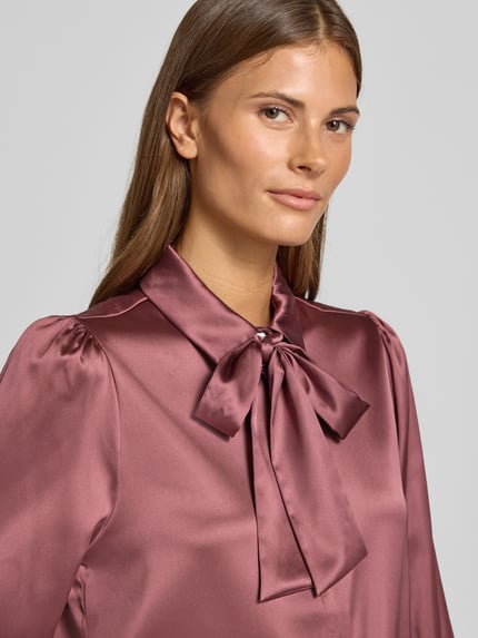 Vrouwenmodel draagt Regular Fit Hemdbluse aus Satin van Christian Berg Woman Selection in bordeaux satijn met sierstrik, close-up bovenlichaam