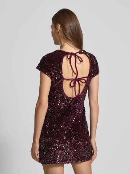 Frauenmodel trägt Minikleid mit Pailletten Modell 'XWILL' von Mango, samtige Struktur, figurbetont, rückenfrei mit Schnürung, Ganzkörperansicht Rückansicht.