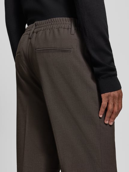 Männermodel trägt Hose mit elastischem Bund und Bügelfalten Modell 'MARC 2.0' von Casual Friday in Dunkelbraun, Detailaufnahme Rückansicht. Material-Mix mit Viskose-Anteil, Regular Fit, Eingrifftaschen, Paspeltaschen am Gesäß, Bundweite 44 cm, Innenbeinlänge 77 cm.