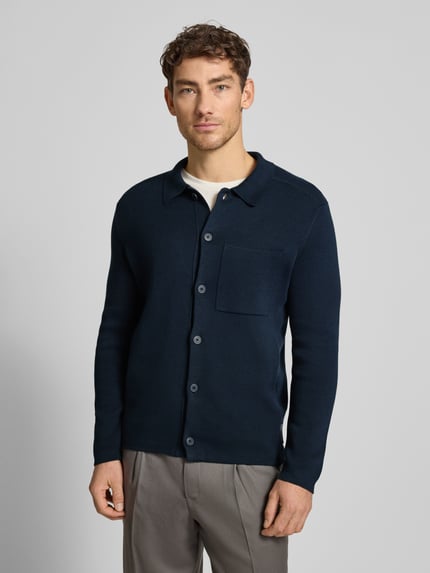Männermodel draagt Regular Fit Strickjacke aus reiner Baumwolle van Marc O'Polo in effen donkerblauw, fijngebreid, borstzak, knoopsluiting, polokraag, geribde boorden, Ganzkörperansicht van voren.
