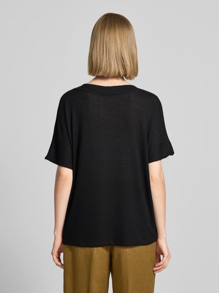 Frauenmodel trägt Strickshirt mit V-Ausschnitt Modell 'Delia' von Soyaconcept in Schwarz, lockere Passform, feine Textur, Rückenansicht, Ganzkörperansicht Rückansicht. Viskose-Mix mit Stretch-Anteil, Rückenlänge 60 cm bei Größe S.
