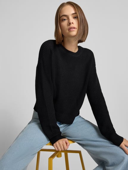 Vrouwenmodel draagt Relaxed Fit Pullover uit katoenmix model 'Maysa' van NOISY MAY®, zwart, grof gebreide structuur, ronde hals, vooraanzicht hele lichaam.