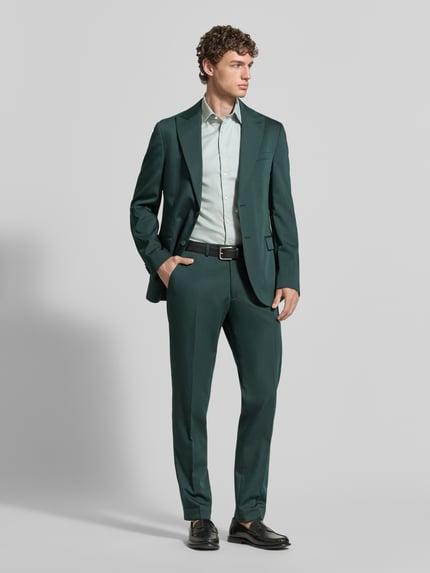 Männermodel trägt Slim Fit Business-Hemd aus Baumwolle mit Kentkragen von Jake*s, hell und glatt, kombiniert mit grünem Anzug, Ganzkörperansicht von vorne.