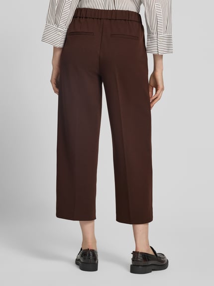 Vrouwenmodel draagt Regular Fit Culotte met viscose van s.Oliver RED LABEL in donkerbruin, gladde textuur, bandplooien, Ganzkörperansicht Rückansicht.