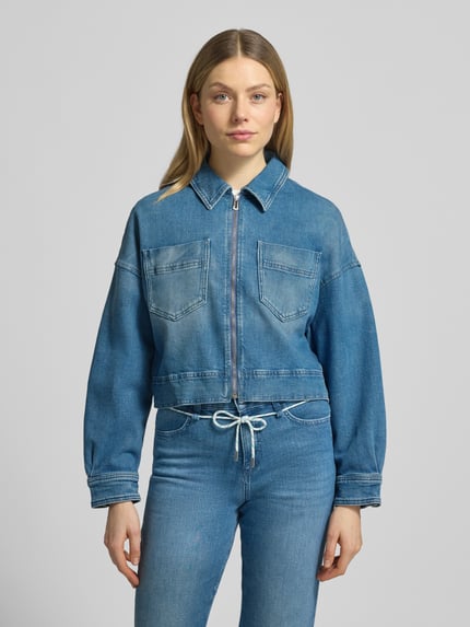 Frauenmodel trägt Cropped Jeansjacke aus Baumwoll-Mix von Marc Cain, gerade Passform, Umlegekragen, Reißverschluss, Brusttaschen, blaue Denim-Optik, mittlere Waschung, glatte Textur, Ganzkörperansicht von vorne.
