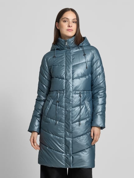 Frauenmodel trägt Steppmantel mit Kapuze Modell 'Jacket-Fa44ncy' von ZABAIONE in glänzendem Metalic-Look mit Taftstruktur, Ganzkörperansicht von vorne.