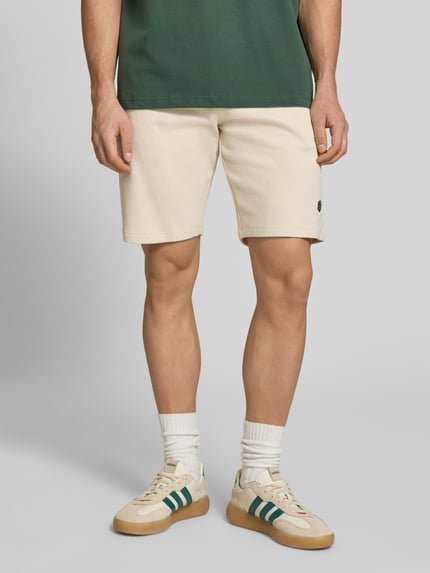 Männermodel trägt Straight Fit Shorts mit Logo-Stitching Modell 'Fillip' von Blend aus Reine Baumwolle mit Strukturmuster, Eingrifftaschen, Gesäßtaschen und elastischem Bund mit Tunnelzug, Ganzkörperansicht von vorne.