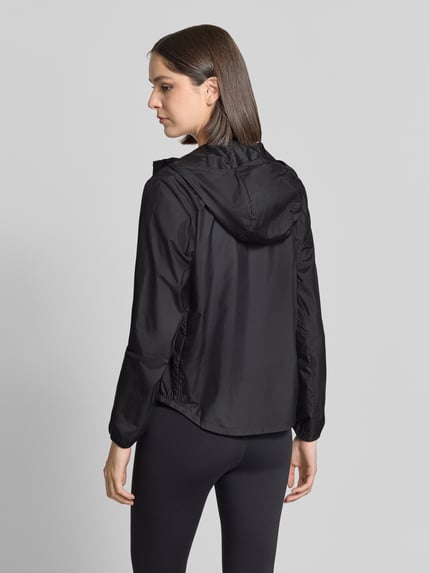 Frauenmodel trägt Jacke mit Logo-Print und Kapuze von ASICS in Schwarz, glatte Textur, elastische Abschlüsse, Ganzkörperansicht Rückansicht. Kontext: Damen Jacke von ASICS, gerader Schnitt, Kapuze, Reißverschluss, Logo-Print, seitliche Eingrifftaschen, elastische Abschlüsse, verlängerter Rücken, Rückenlänge bei Größe S: 61 cm, Schulterbreite bei Größe S: 40 cm, Brustweite bei Größe S: 52 cm, Ärmellänge bei Größe S: 60 cm.