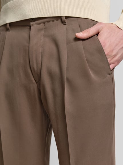 Männermodel trägt Straight Fit Stoffhose aus Lyocell-Mix Modell 'Leek' von Drykorn in Braun mit Bügelfalten, Nahaufnahme Hüftbereich.