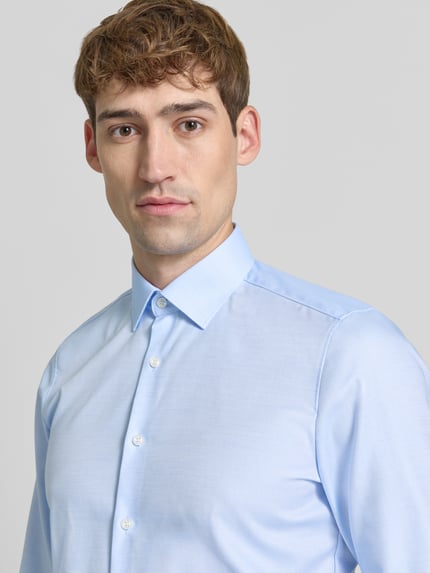 Männermodel trägt Super Slim Fit Businesshemd mit Kentkragen von OLYMP in Hellblau, feine Webstruktur, Nahaufnahme Oberkörper.