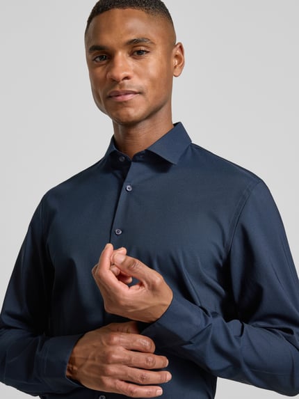 Männermodel trägt dunkelblaues Super Slim Fit Business-Hemd mit Kentkragen von Jake*s, glatte Textur, Nahaufnahme Oberkörper. Material-Mix mit Stretch-Anteil, Knopfleiste, Rückenlänge 78 cm, Schulterbreite 43 cm, Ärmellänge 64 cm.