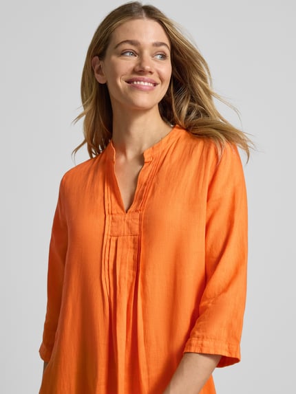 Frauenmodel trägt Tunikakleid aus Leinen mit 3/4-Arm von Emily Van den Bergh in kräftigem Orange, lockerer Schnitt, Nahaufnahme Oberkörper.