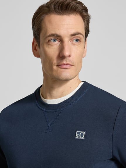 Männermodel trägt Regular Fit Sweatshirt aus Baumwoll-Mix von s.Oliver RED LABEL in Dunkelblau mit Logo-Stitching, Nahaufnahme Oberkörper.