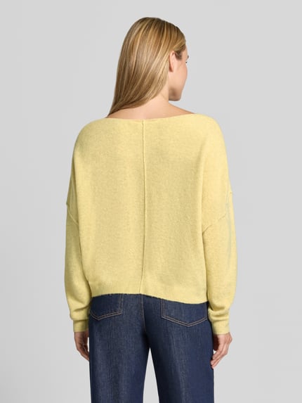 Frauenmodel trägt Relaxed Fit Strickpullover aus Material-Mix mit Leinen-Anteil von American Vintage in Gelb, strukturierte Oberfläche, gerippte Abschlüsse, überschnittene Schultern, Rundhalsausschnitt, Damen Strickpullover, Ganzkörperansicht Rückansicht.