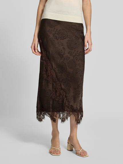 Frauenmodel trägt Midi-Rock mit Spitzenbesatz von VERO MODA in Braun mit floralem Ausbrenner-Effekt, Spitze, asymmetrischem Saum, Nahaufnahme Unterkörper.