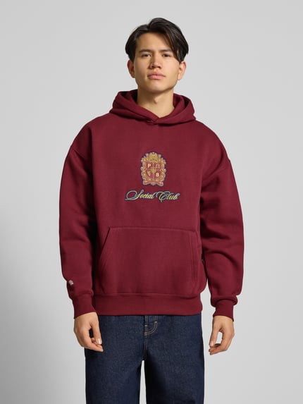 Männermodel trägt Hoodie mit Kapuze von PROHIBITED, bordeauxrot, Baumwoll-Mix, lockerer Schnitt, Känguru-Tasche, Ganzkörperansicht von vorne.