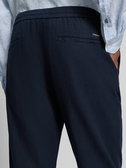 Mannenmodel draagt Jogpants uit mix van katoen en linnen met elastische band van Scotch & Soda, regular fit, detailopname achterzijde. Context: Heren Jogpants van Scotch & Soda, mix van katoen en linnen, regular fit, elastische band, tunnelkoord, bandwijdte bij maat 32/32: 42 cm, binnenbeenlengte bij maat 32/32: 76 cm.