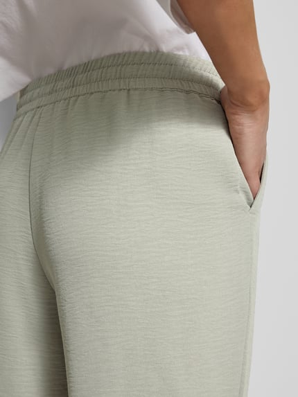 Frauenmodel trägt Jogpants mit elastischem Bund und Eingrifftaschen von Christian Berg Woman in hellgrauer Farbe, Detailaufnahme Rückenpartie. Slim Fit, elastischer Bund mit Kordelzug, französische Eingrifftaschen, Bundweite bei Größe 36: 38 cm, Innenbeinlänge bei Größe 36: 72 cm, leichte Struktur.