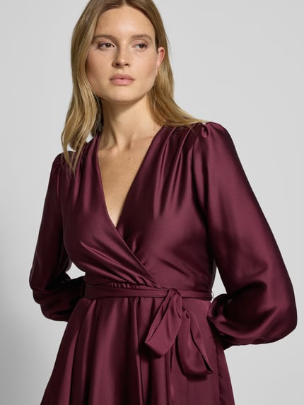 Frauenmodel trägt Cocktailkleid mit Taillengürtel von Swing, V-Ausschnitt, Wickel-Optik, Bordeaux, blickdicht, Nahaufnahme Oberkörper.