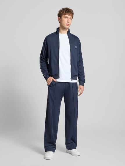 Männermodel trägt Trainingsjacke mit aufgesetztem Band auf Raglanärmeln von REVIEW in Dunkelblau, Regular Fit, Ganzkörperansicht von vorne.