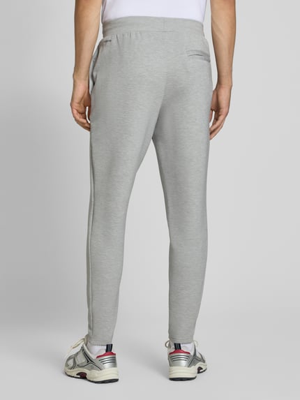 Mężczyznę nosi spodnie dresowe Regular Fit Sweatpants mit Lyocell-Anteil von PUMA PERFORMANCE w szarym kolorze, elastyczna mieszanka materiałów z lyocellem, detal z logo, elastyczny pas z tunelem, elastyczne zakończenia nogawek, Długość wewnętrzna nogawki w rozmiarze M: 76 cm, Ganzkörperansicht Rückansicht.