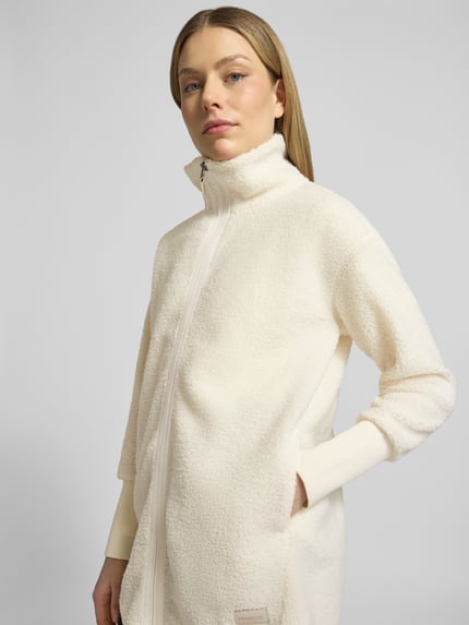 Frauenmodel trägt Fleecejacke mit Stehkragen Modell 'TOLA' von Didriksons in Creme, Relaxed-Fit, Reißverschluss, Nahaufnahme Oberkörper. Rückenlänge bei Größe 36: 83 cm, Schulterbreite: 52 cm, Brustweite: 47 cm, Ärmellänge: 56 cm. Textur weich und flauschig.