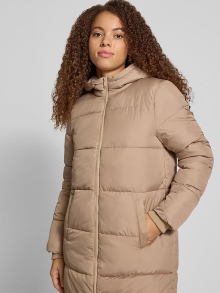 Frauenmodel trägt Puffer Coat mit Kapuze von PIECES in Uni-Beige mit Reißverschluss und Taschen, Longline, seitliche Eingrifftaschen, Langarm, Nahaufnahme Oberkörper.