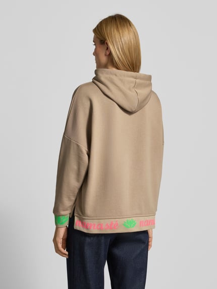 Männermodel trägt Oversized Hoodie mit Strasssteinbesatz Modell 'Namaste' von miss goodlife aus bawełna, krój oversized fit, kaptur z tunelem, nadruk z napisem, wykończenia: elastische Abschlüsse, widok całej sylwetki z tyłu.