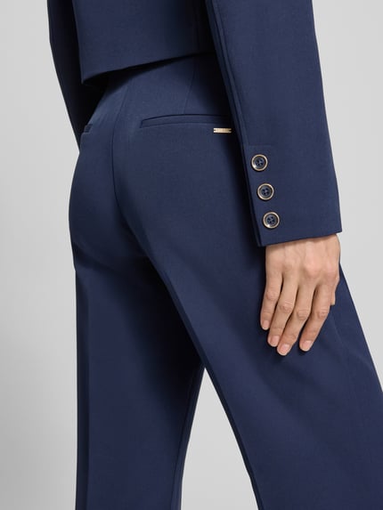 Frauenmodel trägt Hose mit Gürtel Modell 'LEILA' von Guess, Material-Mix mit Stretch-Anteil, Flared-Cut, Detailaufnahme Rückansicht.