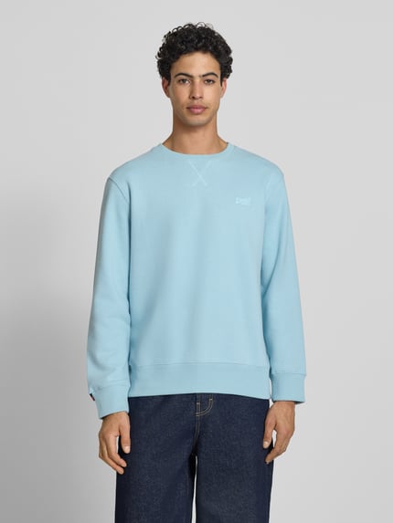Männermodel trägt Sweatshirt mit Rundhalsausschnitt und Label-Stitching von Superdry in Hellblau, Baumwoll-Mix, Regular-Fit, Ganzkörperansicht von vorne.